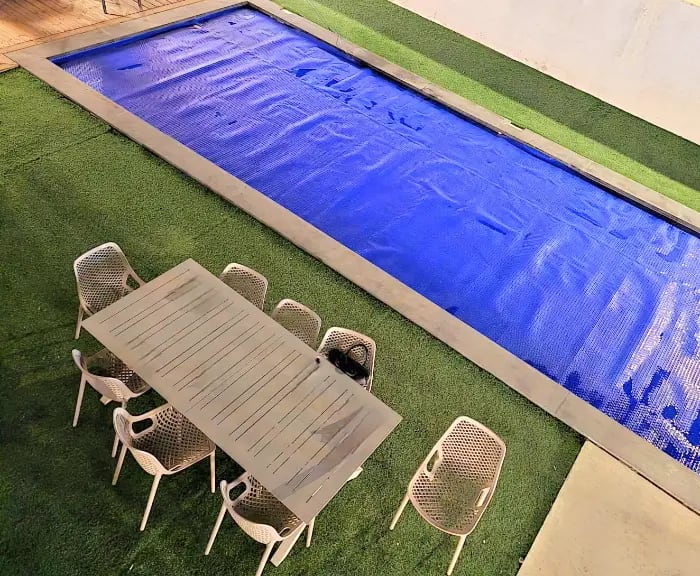 בריכת המתחם לצד פינת אוכל חיצונית עם כיסאות לבנים על דשא